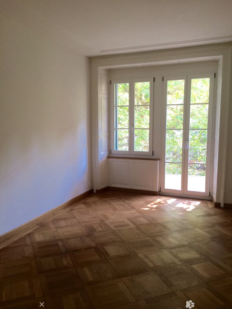 Empty room with wooden flooring, white walls, large windows, and a radiator cover.