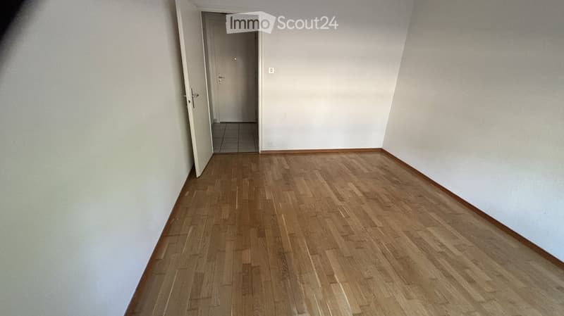 Empty room with wooden flooring and white walls, featuring an open doorway leading to another tiled area.
