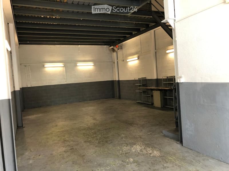 Empty room with concrete floor, white and gray walls, metal shelving units, and a staircase leading upwards.