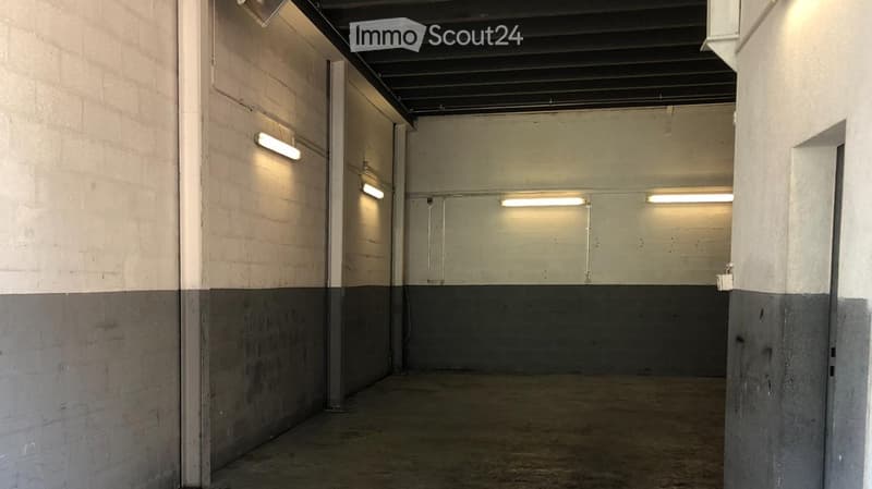 Empty room with concrete floor, white and grey walls, fluorescent lighting, and a closed door.