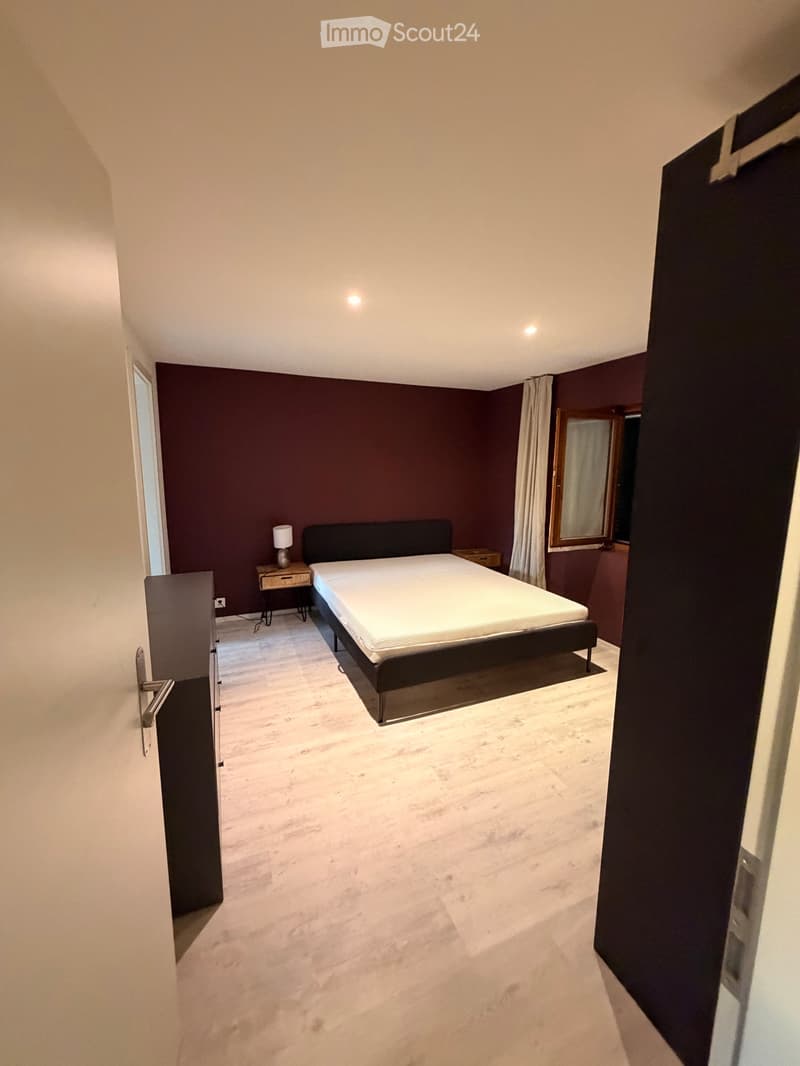 Modern bedroom with dark walls, white bedding, marble flooring, and a nightstand with a lamp.