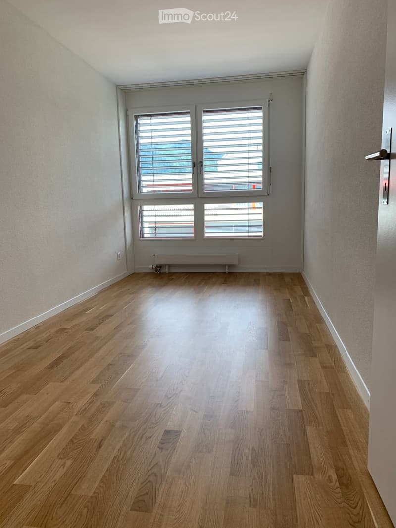 Empty room with wooden flooring, white walls, and large windows with blinds. No furniture or equipment present.