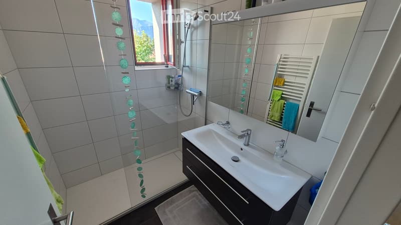 Modern bathroom with a double sink, large mirror, glass-enclosed shower, and towel rack with towels.