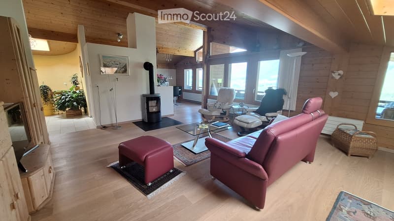 Bright living room with wooden floors, exposed wooden beams, large windows, red leather sofa, ottoman, coffee table, fireplace, and decorative items.