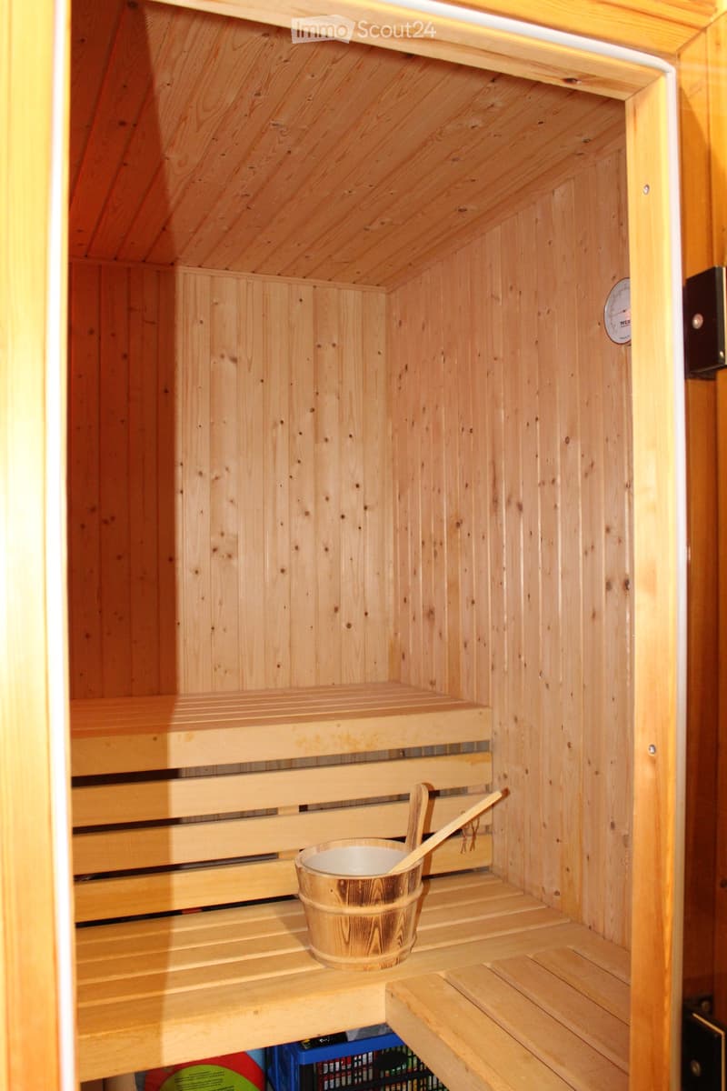 Wooden sauna interior with benches, a bucket, and a wooden spoon, featuring light wooden walls and a slanted ceiling.