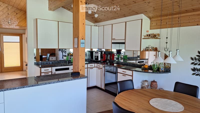 Modern kitchen with white cabinets, granite countertops, and a wooden dining table with chairs. Features include a coffee maker, blender, and various appliances.