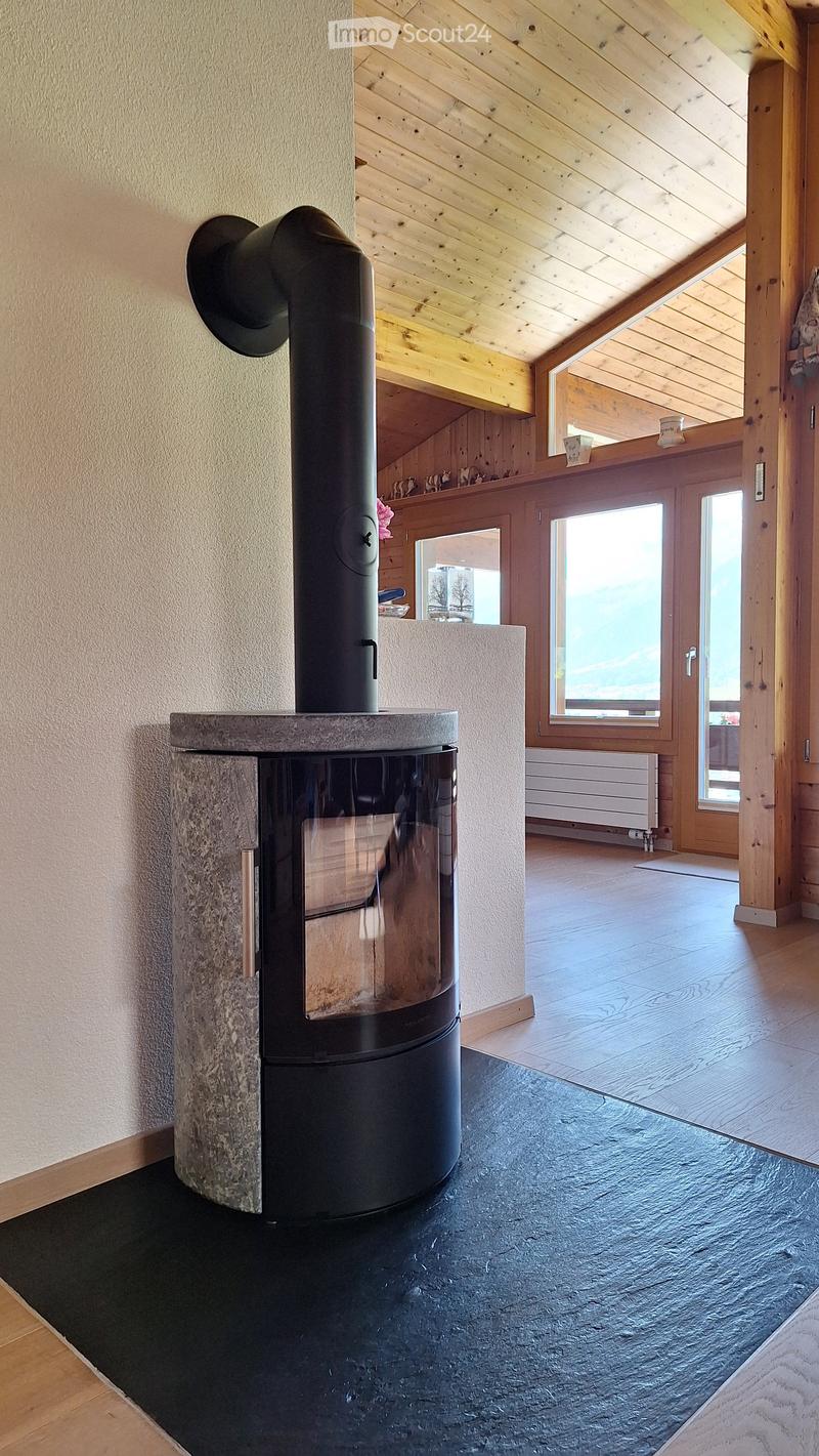 Modern living room with a sleek black wood-burning stove, wooden ceiling beams, large windows, and wooden flooring.