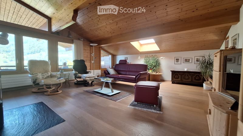 Bright living room with wooden ceiling and floors, large windows, a red leather sofa, a glass coffee table, a white rocking chair, and a small table with a plant.