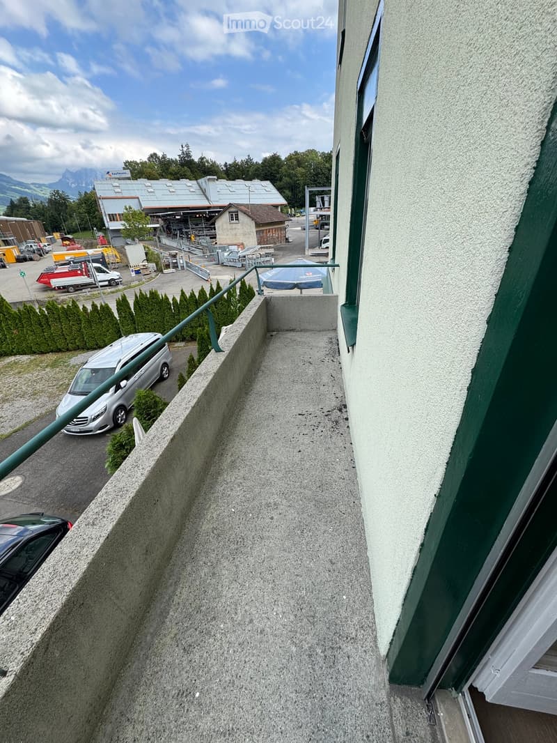 Balcony with concrete floor, green railing, overlooking a parking area with cars and construction site.