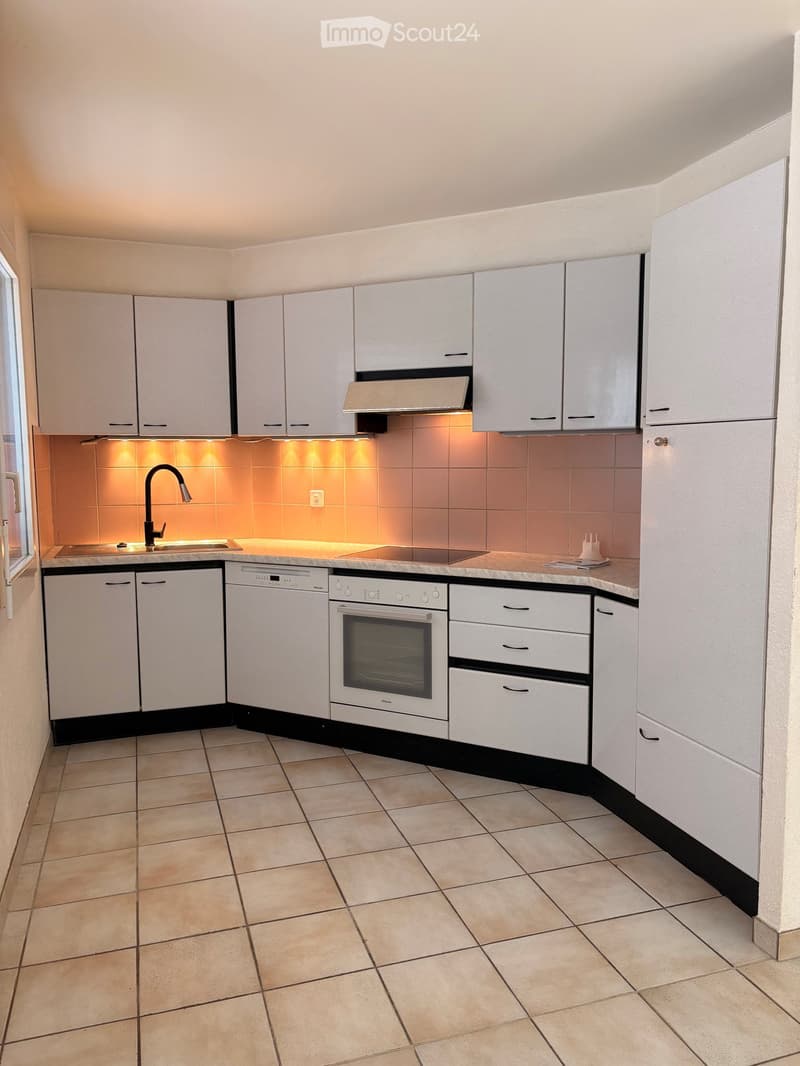 Modern kitchen with white cabinets, stainless steel appliances, and a warm backsplash. Features include a sink with a modern faucet, an oven, a dishwasher, and a refrigerator.