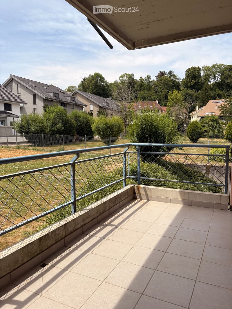 Balcony with tiled floor, metal railing, and view of a residential area with houses and greenery.