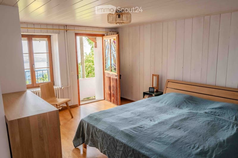 Cozy bedroom with wooden walls and floor, a large bed with blue bedding, a wooden chair, a small table with a mirror, and a radiator near the window.
