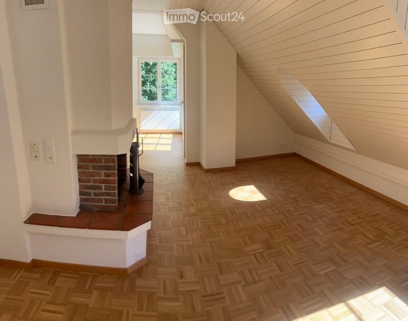 Empty room with wooden herringbone flooring, white walls, and a brick fireplace. Sunlight streams in from a large window and skylight.
