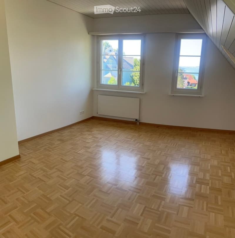 Empty room with wooden herringbone flooring, white walls, and large windows offering a view of the outside. No furniture or equipment present.