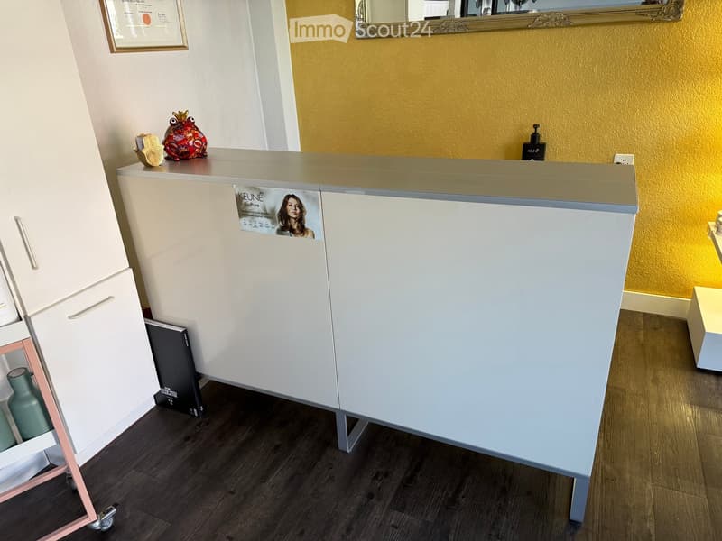 Modern reception area with a sleek white reception desk, framed certificate, decorative vase, mirror, and a poster on the wall.