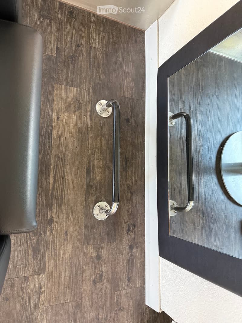Close-up view of a hallway with wooden flooring, a door handle, and a mirror with a dark frame mounted on the wall.