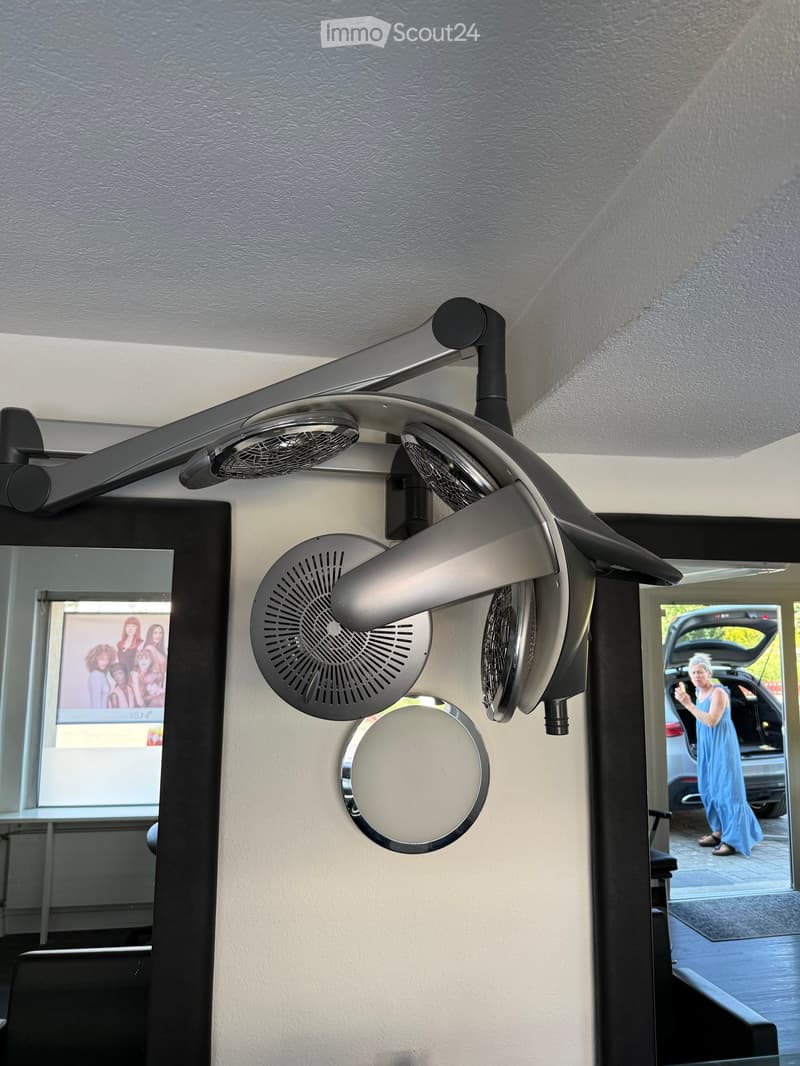A modern salon setup with a large, multi-head fan and a round mirror mounted on the wall, with a poster visible in the background.