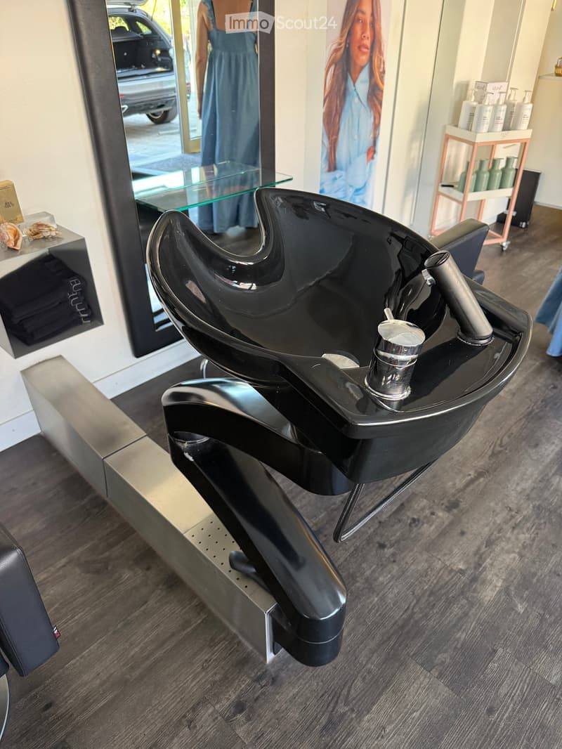 Modern salon interior with a black salon chair, sink, and various hair care products on shelves.