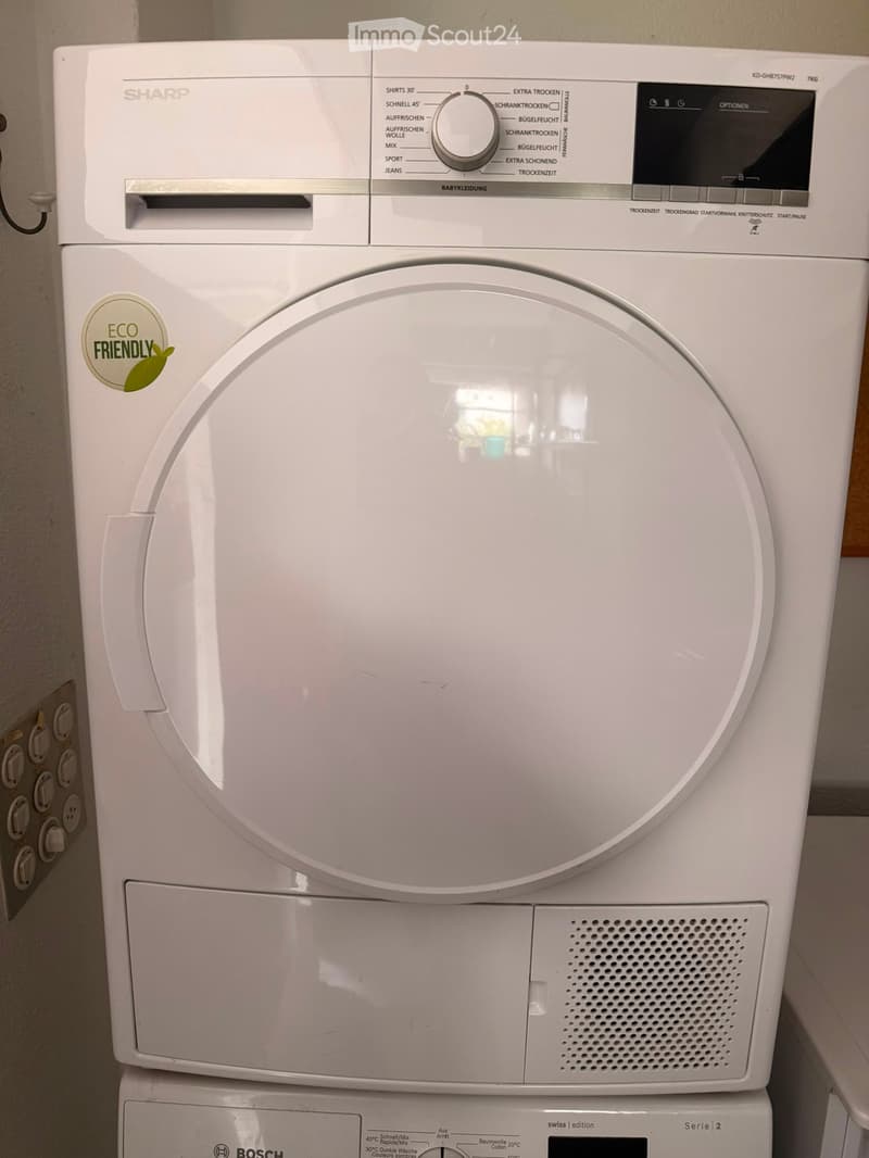 A white Bosch washing machine and a Sharp dryer are stacked vertically in a bathroom setting.