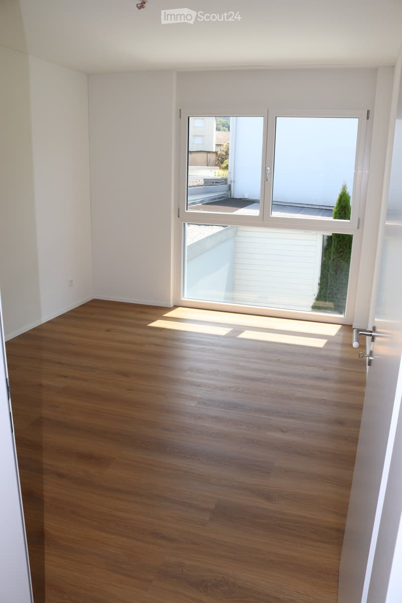 Empty room with wooden flooring, white walls, and large glass sliding doors leading to a balcony or outdoor area.