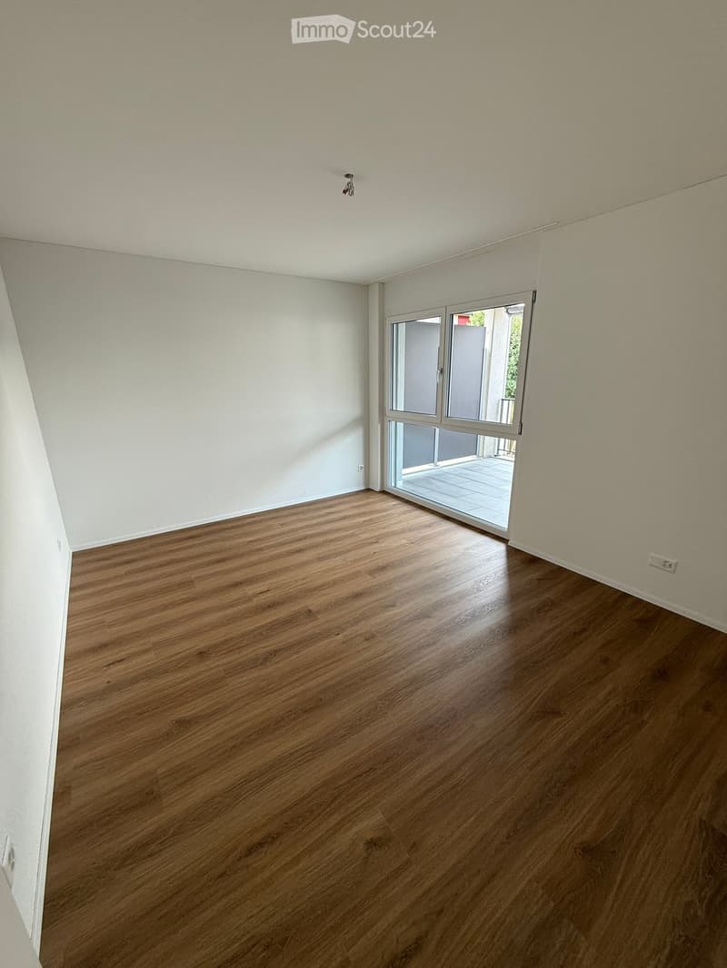 Empty room with wooden flooring and white walls, featuring a large sliding glass door leading to an outdoor area.