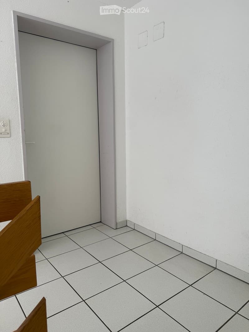 Empty room with white tiled floor and white walls, featuring a doorway and a partially visible wooden cabinet.