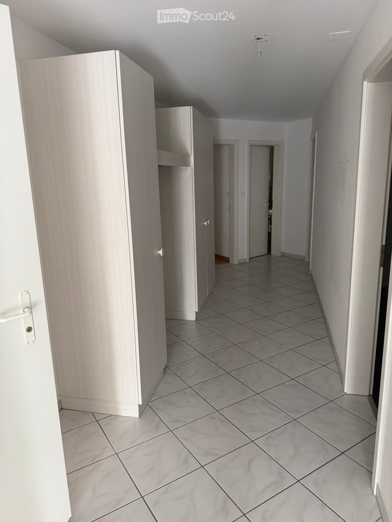 Empty hallway with tiled floor, white walls, and several doors leading to other rooms.