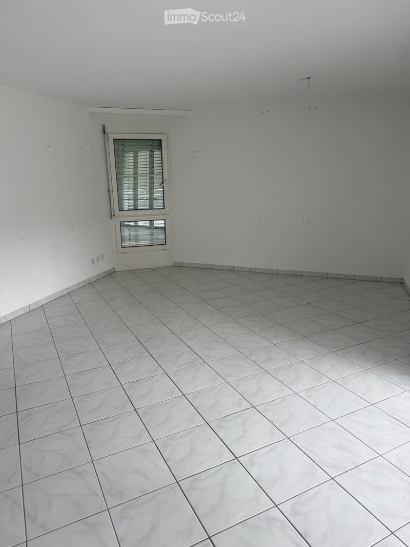 Empty room with white walls, tiled floor, and a single window with blinds.