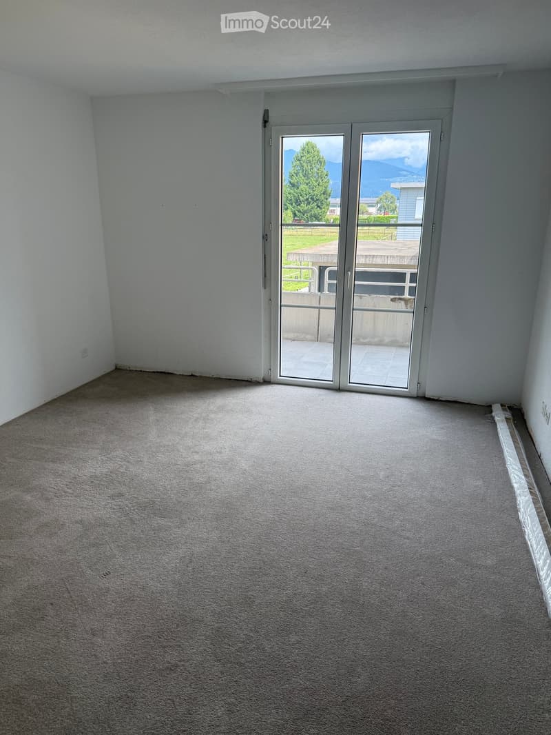 Empty room with light grey carpeting, white walls, and a large sliding glass door leading to a balcony with a scenic mountain view.