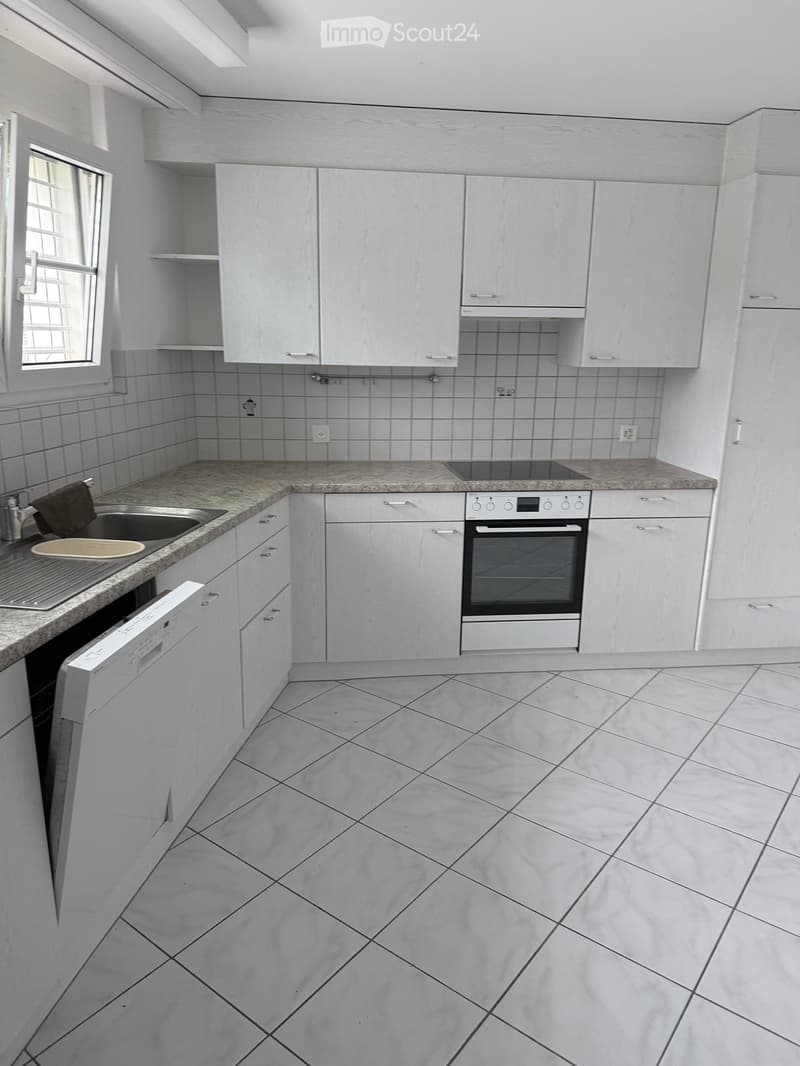 Modern kitchen with white cabinets, granite countertop, sink, oven, and dishwasher. Light grey tiled floor and walls.