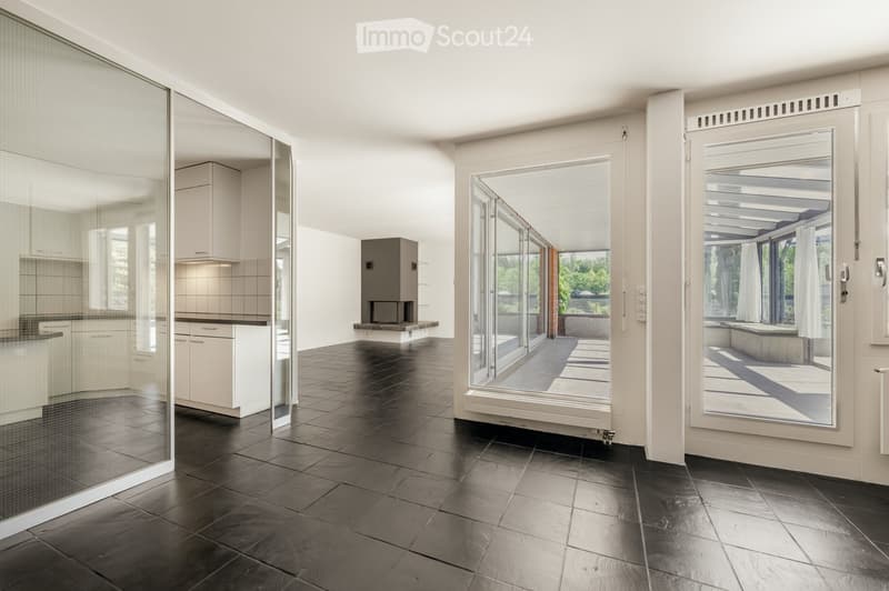Open-plan space with dark tiled flooring, large glass sliding doors leading to a covered outdoor area, and a small kitchen area visible on the left side.