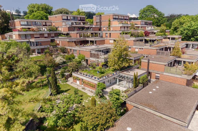 Aerial view of a modern residential complex with multiple interconnected buildings, surrounded by lush greenery and well-maintained gardens.