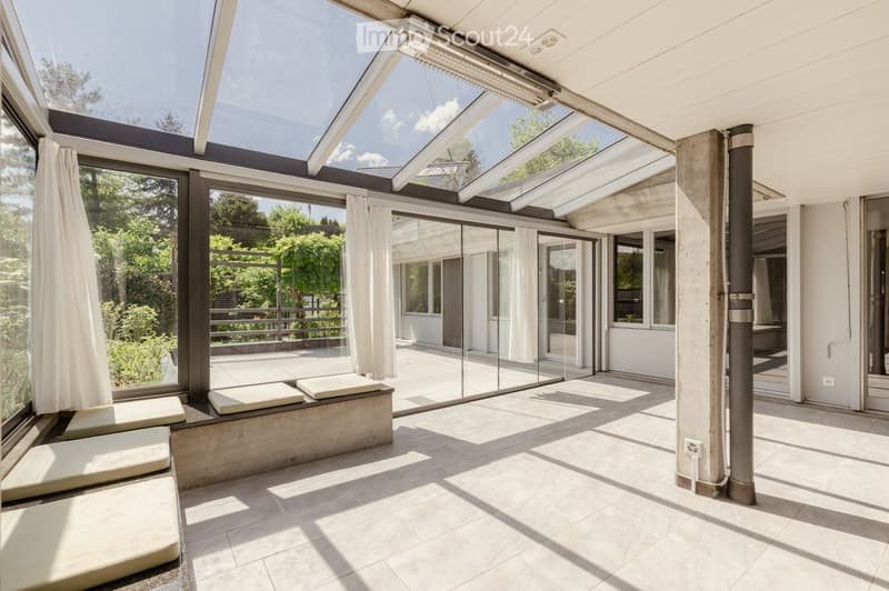 Bright, modern sunroom with large glass walls and a retractable roof, featuring a built-in concrete bench seating area.