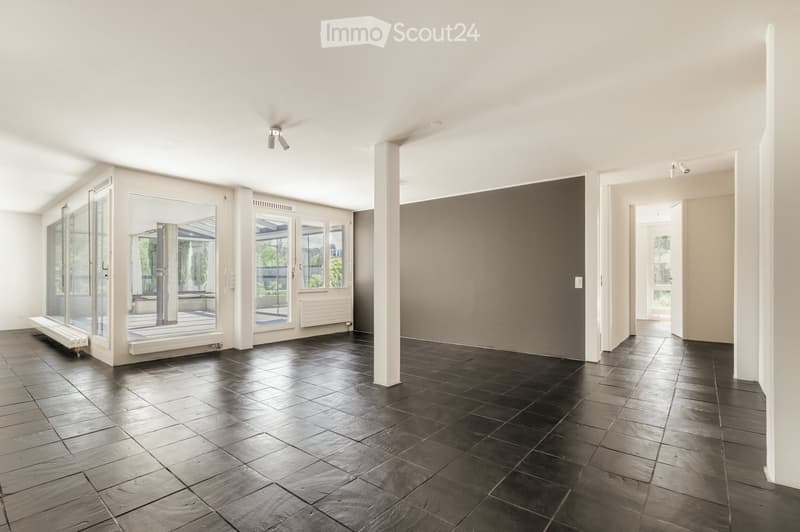 Empty room with dark tiled floor, white walls, large windows, and a central column. No furniture or equipment present.