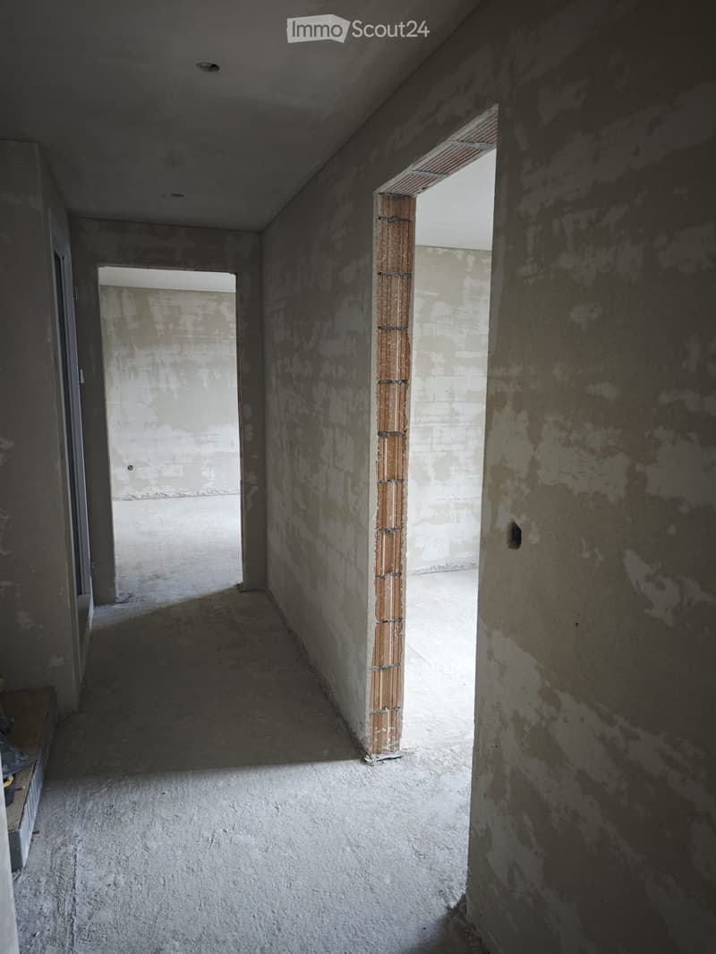 Empty hallway with unfinished concrete walls and floor, featuring a central wooden post and two open doorways leading to other spaces.