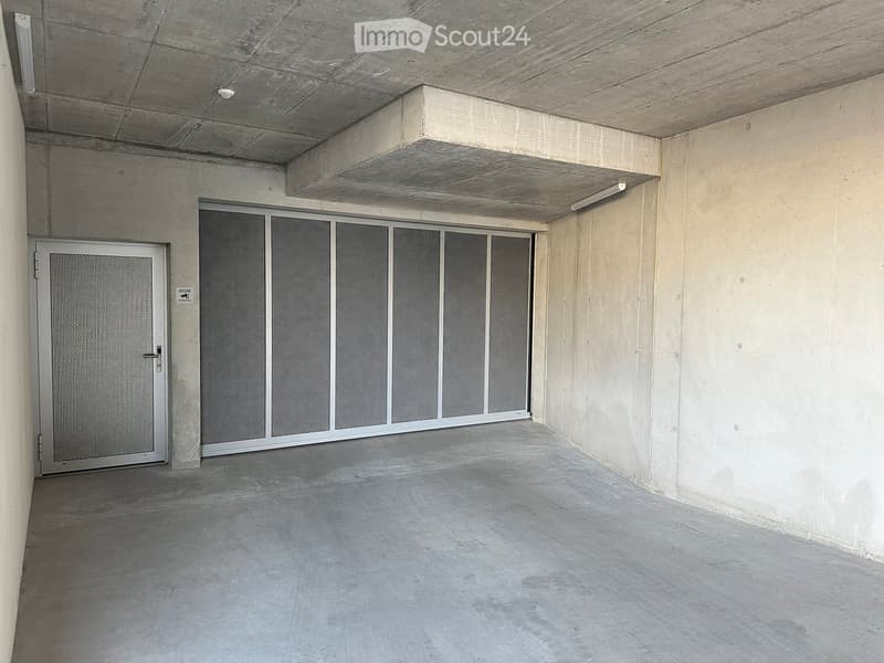 Empty concrete corridor with a large sliding door and a smaller metal door on the left, featuring a smooth concrete floor and walls.