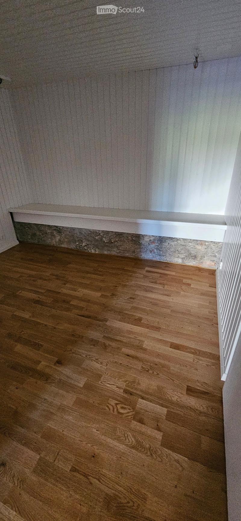 Empty room with wooden flooring and white walls, featuring a window and a small shelf on the wall.