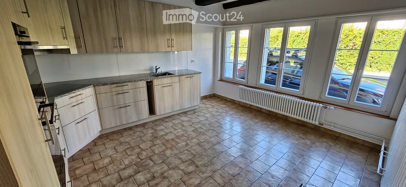 Empty kitchen with light wooden cabinets, granite countertop, sink, and large windows overlooking a parking area.