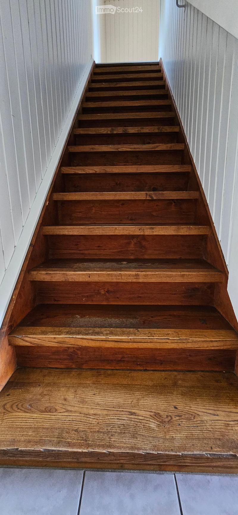 Wooden staircase with open risers and handrails, leading up from a wooden floor area to a higher level.