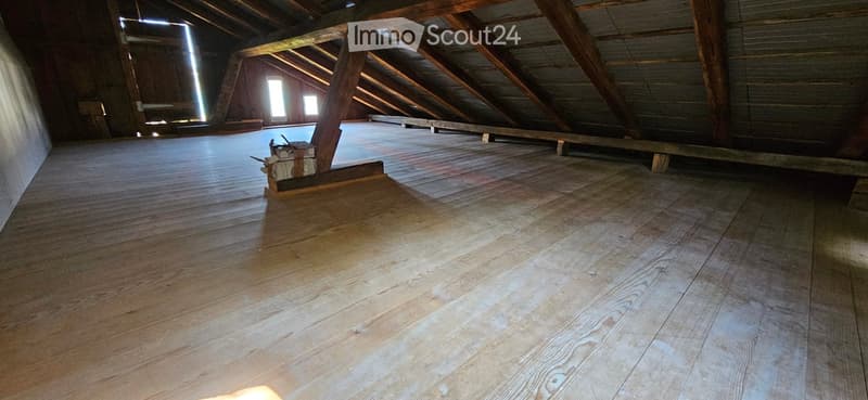 Empty attic space with wooden floors and exposed wooden beams, featuring natural light from small windows.