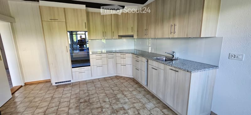 Modern kitchen with light wood cabinets, granite countertop, and stainless steel sink.
