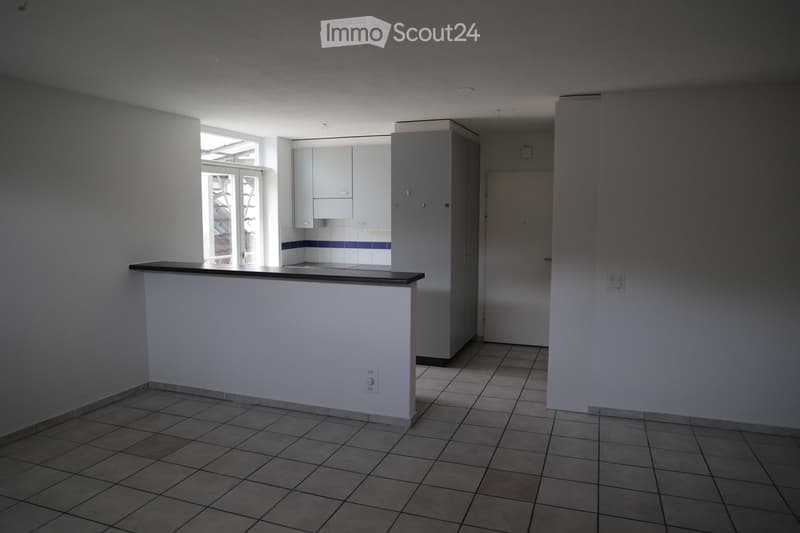 Empty kitchen with tiled floor, white walls, built-in cabinets, and a countertop. No appliances or furniture are present.