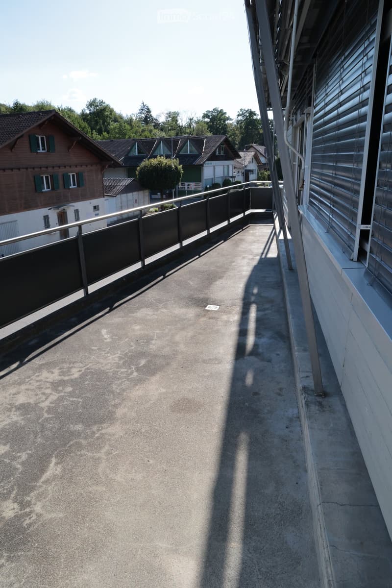 Balcony with metal railing, concrete floor, and view of neighboring houses and greenery.