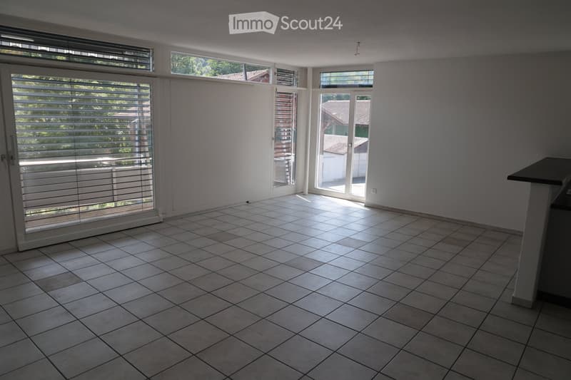 Empty room with tiled floor, large windows with blinds, and a small table in the corner.