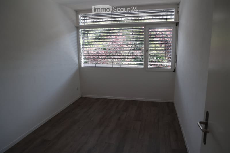 Empty room with wooden flooring, white walls, and large windows with blinds. No furniture or equipment present.