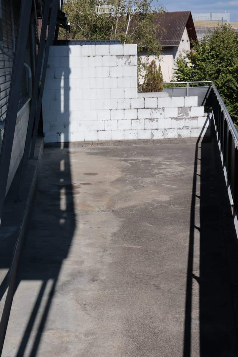 Empty concrete balcony with white brick wall, metal railing, and distant greenery.