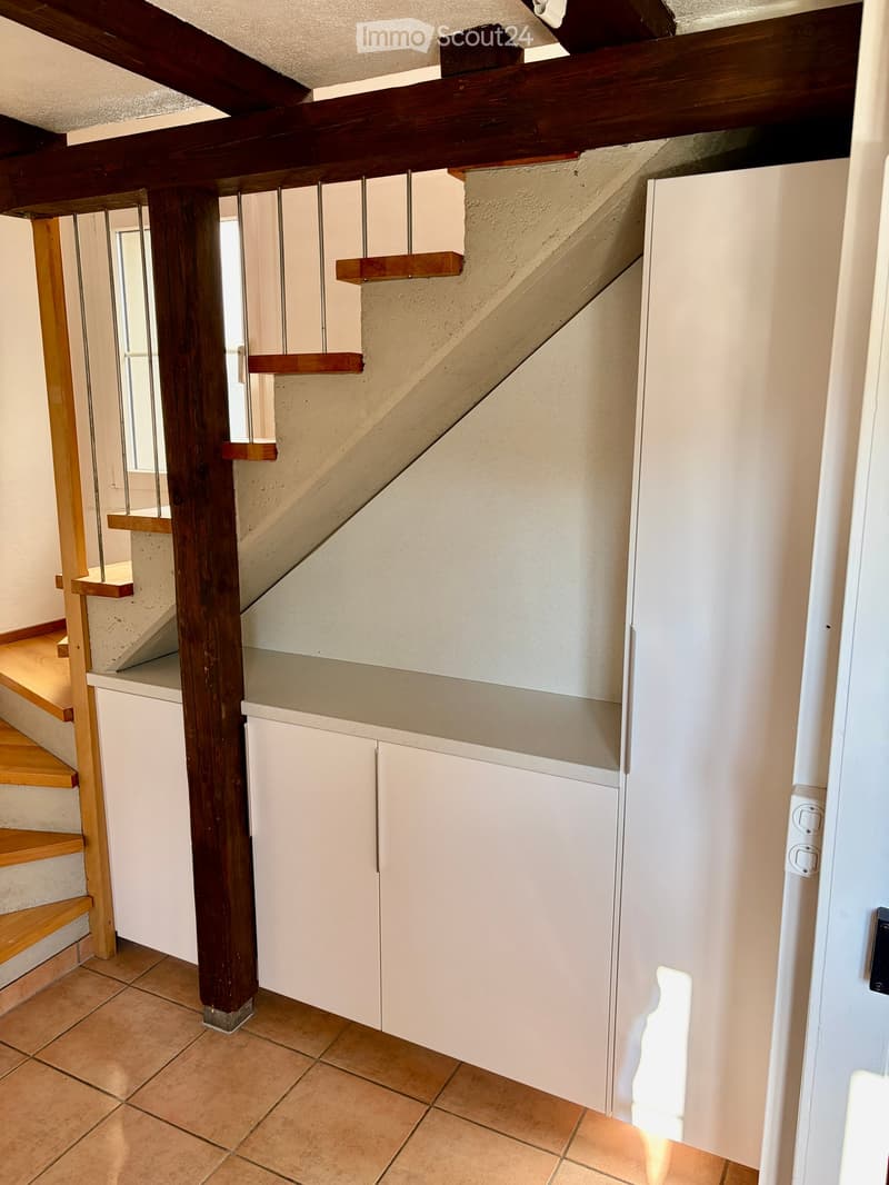 Hallway with wooden staircase, white walls, tiled floor, and built-in white cabinetry.