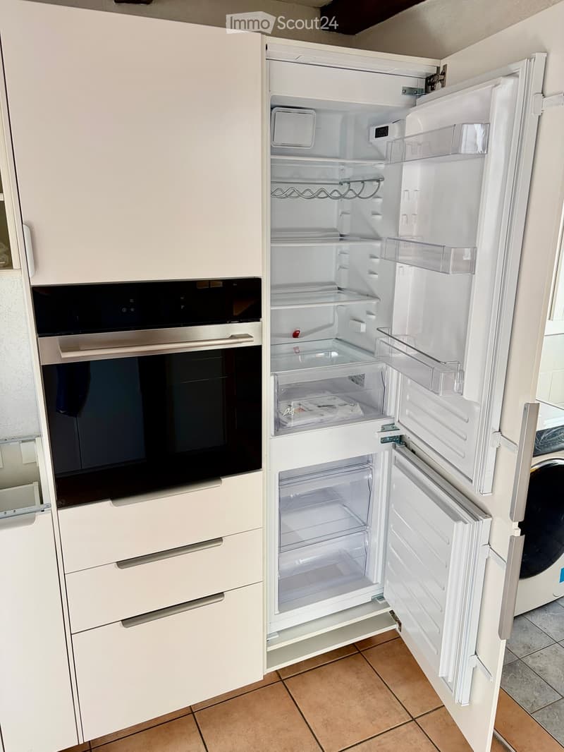 Modern kitchen with white cabinets, a stainless steel oven, and an open refrigerator showing empty shelves and drawers.