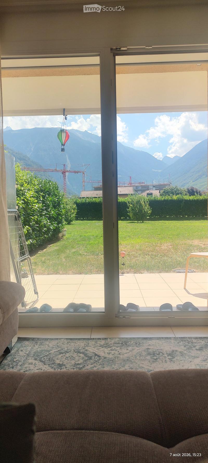 Living room with a sofa, patterned rug, large windows offering a scenic mountain view, and a small table on the balcony.