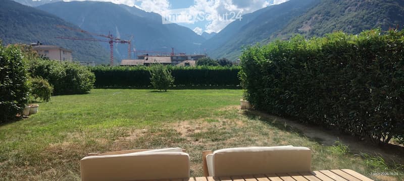 Lush garden with green grass, trimmed hedges, and a scenic mountain view in the background.
